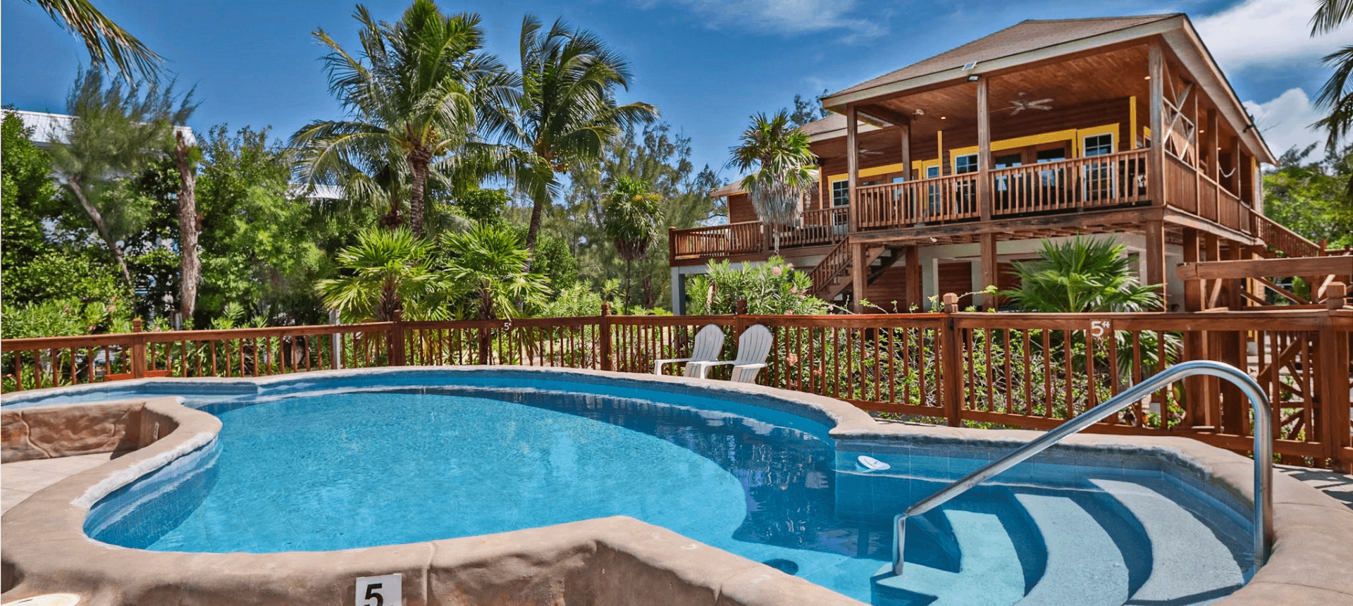 Tropical poolside with wooden deck and house.